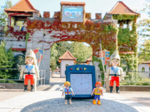 Two PLAYMOBIL-Figures with an alarm clock in front of the PLAYMOBIL-FunPark's entrance